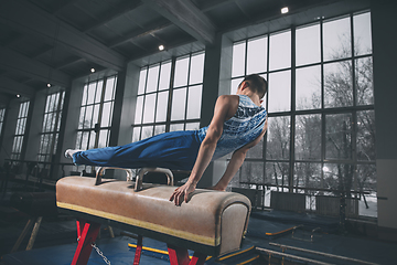 Image showing Little male gymnast training in gym, flexible and active. Caucasian fit little boy, athlete in sportswear practicing in exercises for strength, balance.