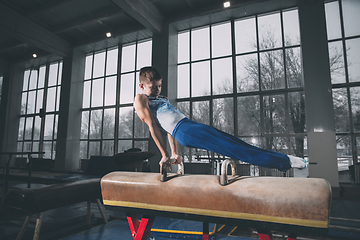 Image showing Little male gymnast training in gym, flexible and active. Caucasian fit little boy, athlete in sportswear practicing in exercises for strength, balance.