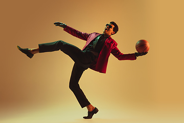 Image showing High-fashion styled man in red jacket playing basketball isolted over brown background