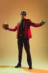 Image showing High-fashion styled man in red jacket playing basketball isolted over brown background