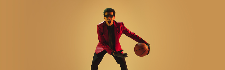 Image showing High-fashion styled man in red jacket playing basketball isolted over brown background