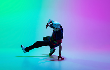 Image showing Beautiful sportive boy dancing hip-hop in stylish clothes on colorful gradient background at dance hall in neon light.