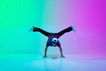 Image showing Beautiful sportive boy dancing hip-hop in stylish clothes on colorful gradient background at dance hall in neon light.