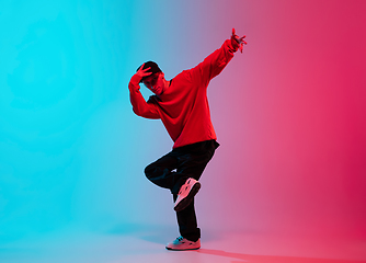 Image showing Beautiful sportive boy dancing hip-hop in stylish clothes on colorful gradient background at dance hall in neon light.