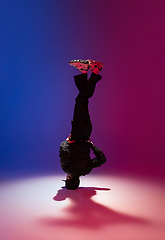 Image showing Beautiful sportive boy dancing hip-hop in stylish clothes on colorful gradient background at dance hall in neon light.