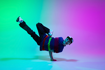 Image showing Beautiful sportive boy dancing hip-hop in stylish clothes on colorful gradient background at dance hall in neon light.