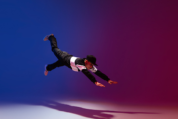 Image showing Beautiful sportive boy dancing hip-hop in stylish clothes on colorful gradient background at dance hall in neon light.