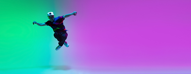 Image showing Beautiful sportive boy dancing hip-hop in stylish clothes on colorful gradient background at dance hall in neon light.