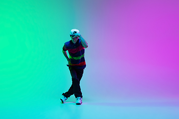 Image showing Beautiful sportive boy dancing hip-hop in stylish clothes on colorful gradient background at dance hall in neon light.