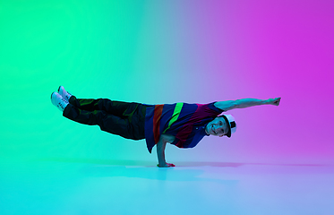 Image showing Beautiful sportive boy dancing hip-hop in stylish clothes on colorful gradient background at dance hall in neon light.