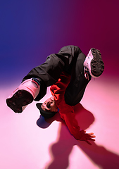 Image showing Beautiful sportive boy dancing hip-hop in stylish clothes on colorful gradient background at dance hall in neon light.