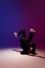 Image showing Beautiful sportive boy dancing hip-hop in stylish clothes on colorful gradient background at dance hall in neon light.