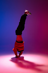 Image showing Beautiful sportive boy dancing hip-hop in stylish clothes on colorful gradient background at dance hall in neon light.