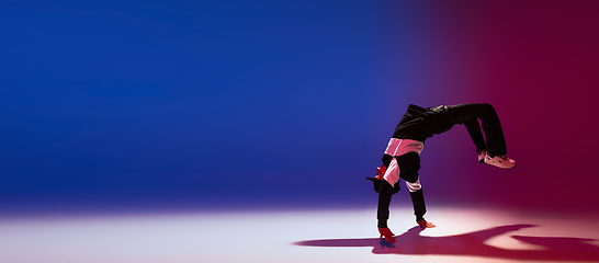 Image showing Beautiful sportive boy dancing hip-hop in stylish clothes on colorful gradient background at dance hall in neon light.