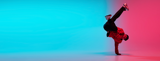 Image showing Beautiful sportive boy dancing hip-hop in stylish clothes on colorful gradient background at dance hall in neon light.