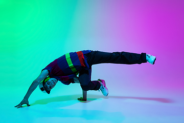 Image showing Beautiful sportive boy dancing hip-hop in stylish clothes on colorful gradient background at dance hall in neon light.