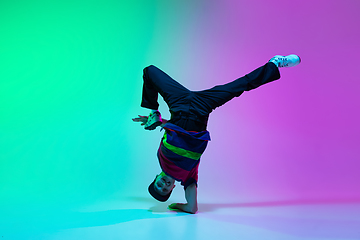 Image showing Beautiful sportive boy dancing hip-hop in stylish clothes on colorful gradient background at dance hall in neon light.