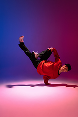 Image showing Beautiful sportive boy dancing hip-hop in stylish clothes on colorful gradient background at dance hall in neon light.