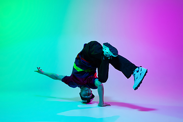 Image showing Beautiful sportive boy dancing hip-hop in stylish clothes on colorful gradient background at dance hall in neon light.