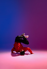 Image showing Beautiful sportive boy dancing hip-hop in stylish clothes on colorful gradient background at dance hall in neon light.