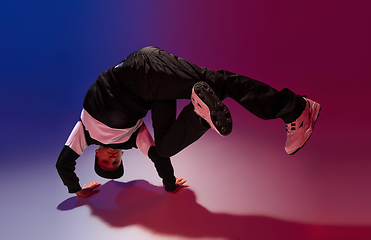 Image showing Beautiful sportive boy dancing hip-hop in stylish clothes on colorful gradient background at dance hall in neon light.