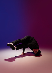 Image showing Beautiful sportive boy dancing hip-hop in stylish clothes on colorful gradient background at dance hall in neon light.