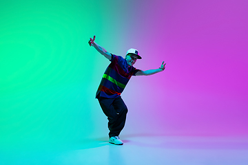 Image showing Beautiful sportive boy dancing hip-hop in stylish clothes on colorful gradient background at dance hall in neon light.