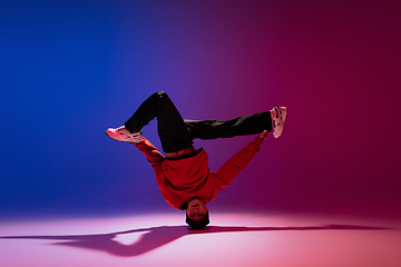 Image showing Beautiful sportive boy dancing hip-hop in stylish clothes on colorful gradient background at dance hall in neon light.