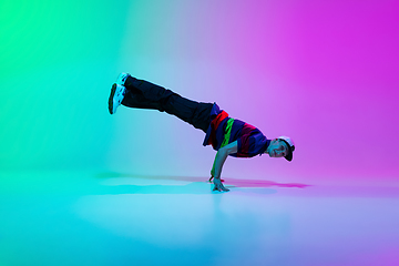 Image showing Beautiful sportive boy dancing hip-hop in stylish clothes on colorful gradient background at dance hall in neon light.