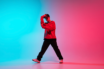 Image showing Beautiful sportive boy dancing hip-hop in stylish clothes on colorful gradient background at dance hall in neon light.