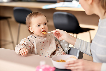 Image showing happy mother feeding baby with puree at home