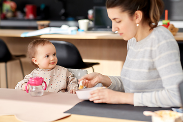 Image showing happy mother feeding baby with puree at home