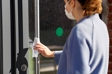 Image showing woman in mask cleaning door handle with wet wipe