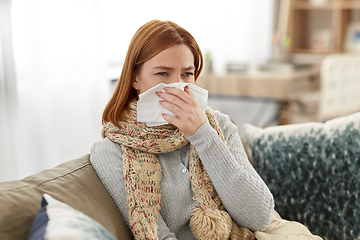 Image showing sick woman blowing nose in paper tissue at home