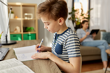 Image showing student boy with book writing to notebook at home