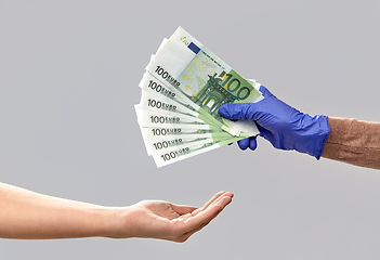 Image showing one hand in medical glove giving money to another