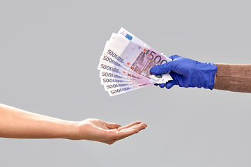 Image showing one hand in medical glove giving money to another