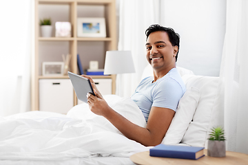 Image showing happy indian man with tablet pc in bed at home