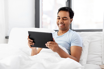 Image showing happy indian man with tablet pc in bed at home