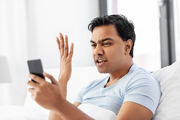 Image showing angry indian man with smartphone in bed at home