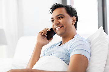 Image showing happy indian man calling on smartphone in bed