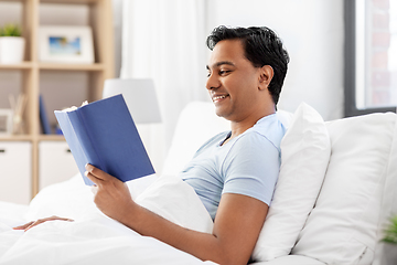 Image showing happy indian man reading book in bed at home