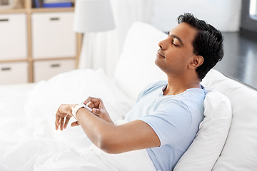 Image showing happy indian man with smart watch in bed at home