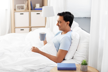 Image showing happy indian man drinking coffee in bed at home