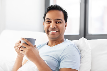 Image showing happy indian man drinking coffee in bed at home