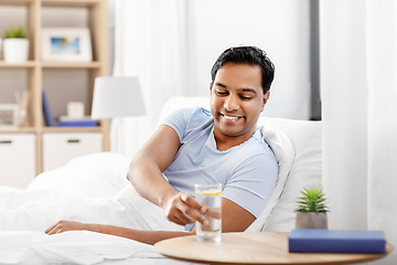 Image showing happy indian man drinking water lying in bed