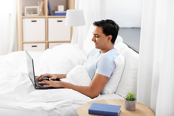 Image showing happy indian man with laptop in bed at home