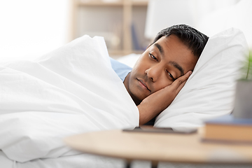 Image showing sleepy indian man in bed looking at smartphone