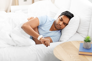 Image showing indian man looking at smart watch in bed at home