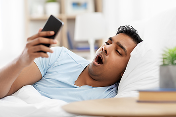 Image showing sleepy indian man with smartphone lying in bed